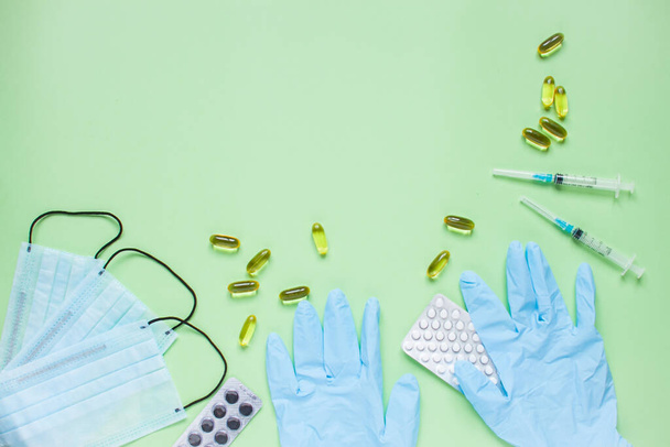 Surgical medical face masks, rubber protective gloves, syringes and pills. Coronavirus, protection concept. Global pandemic. Medicine. Layout. Green background - Photo, image