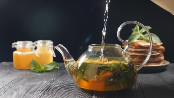 Kaynar suyla çay demliyorum. Arkaplanda bal ve krep yığını var. Çay yapraklarına su ve cam çaydanlığa portakal dilimleri ekliyorum. Çay yapıyorum. Matcha Çay Töreni. Tam Hd - Video, Çekim