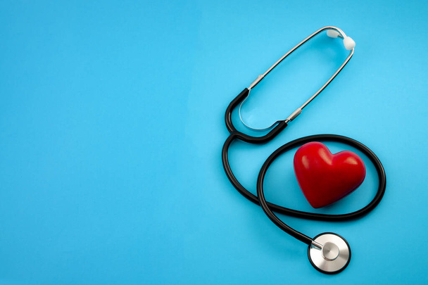 Yearly health check up, disease diagnosis medicine, healthcare and cardiology concept with a red heart and a stethoscope isolated on a hospital blue background with copy space - Photo, Image