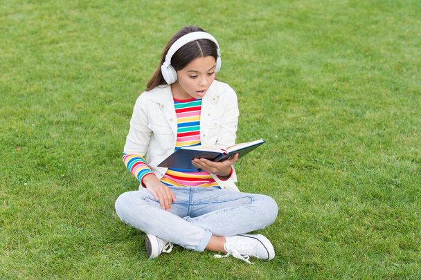 存在するための素晴らしい場所。デジタルライフにおける新技術です。知識の日だ。将来の学校教育です。緑の草の本を持つ10代の少女。可愛い娘が本を読んでる。子供向けの文学を研究し - 写真・画像