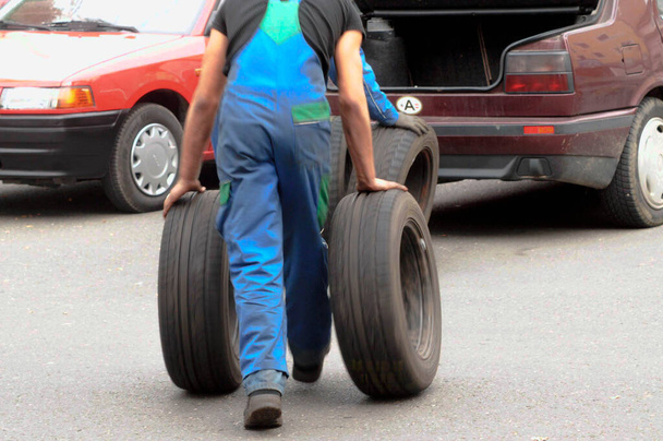 zaměstnanec autoservisu ručně vyměňuje pneumatiky na vozidle - Fotografie, Obrázek