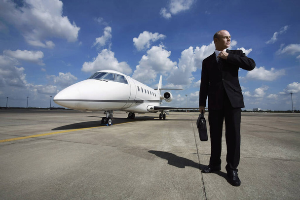 Businessman adjusting his tie on runway with private jet in the background - Foto, afbeelding