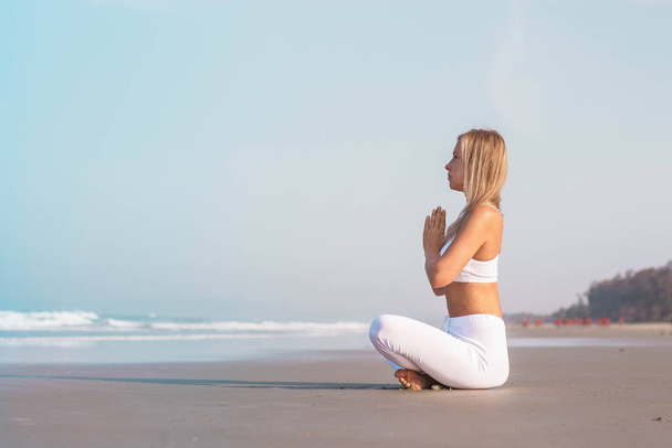 a beautiful girl in white clothes is sitting on the ocean and practicing yoga and meditation - Foto, Bild