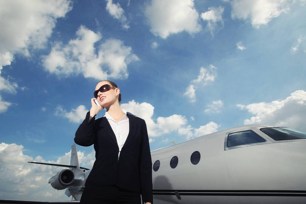 Businesswoman talking on the phone with private jet in the background - Foto, afbeelding