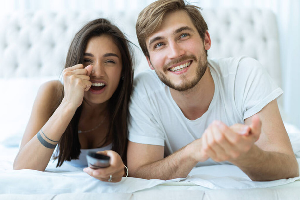 happy couple with remote lying in bed at home and watching tv. - Photo, image