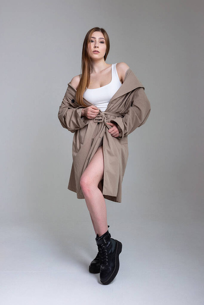 attractive caucasian skinny girl in raincoat posing on white studio cyclorama - Fotó, kép