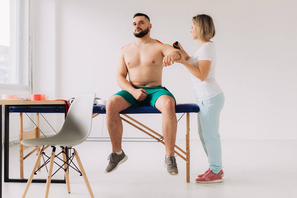 Fisioterapista che applica il nastro Kinesio ai pazienti feriti alla spalla - Foto, immagini