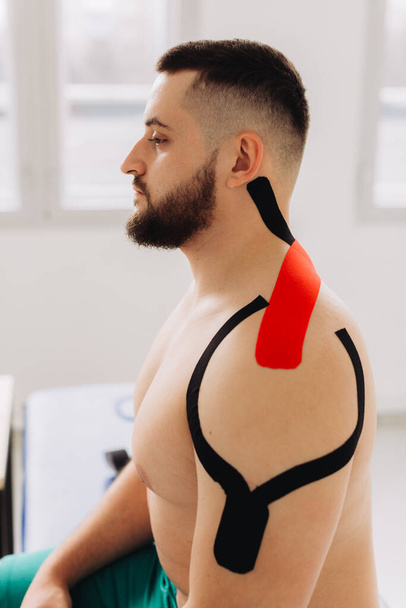 Close-up man lifting his arms. Sportsman having kinesio tape on his shoulder and arm after workout injury at gym. Close up on bicep muscles of a professional athlete - Photo, image