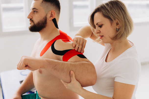 Физиотерапевт, применяющий ленту Кинезио к пациентам с травмой плеча - Фото, изображение