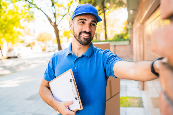 Portrait of a delivery man carrying packages while ringing house doorbell for making home delivery to his customer. Delivery and shipping concept. - Foto, Imagen