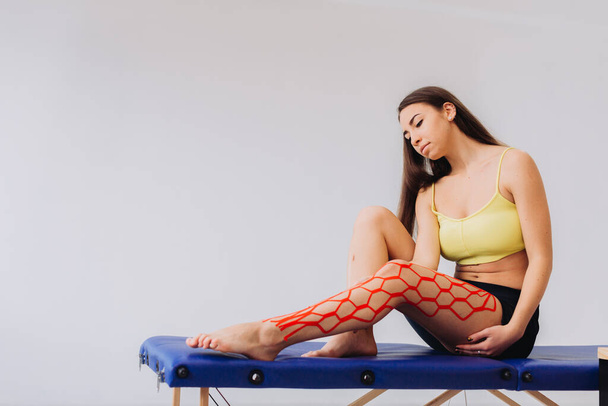 Menina bonito colocando fita cinesio elástico em seu joelho e perna. Cinesiologia, fisioterapia, conceito de reabilitação - Foto, Imagem