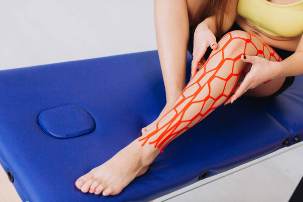 Young sportive female athlete holding her injured leg after treatment with kinesio tape. Kinesiology, physical therapy, rehabilitation concept - Foto, Imagen