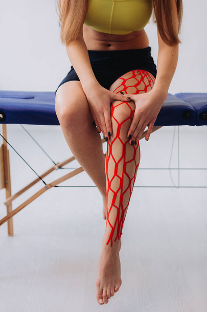 Fiatal sportoló női sportoló tartja a sérült lábát kinesio-szalaggal végzett kezelés után. Kineziológia, fizikoterápia, rehabilitációs koncepció - Fotó, kép