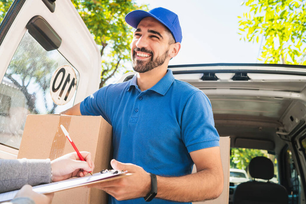 Portrait of a delivery man carrying packages while customer putting signature in clipboard. Delivery and shipping concept. - Foto, imagen