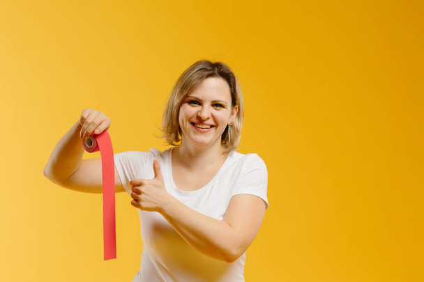 A therapist rolling kinesiology tape to demonstrate it on the yellow background. Alternative kinesio tape therapy, healthcare concept - Photo, Image