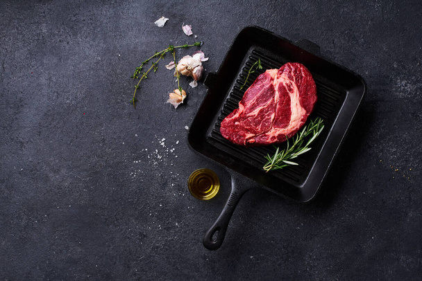 Black Angus prime beef chuck roll steak on cast iron grill skillet with fresh rosemary and olive oil with garlic. Creative layout with cooking ingredients, Top view - Fotoğraf, Görsel