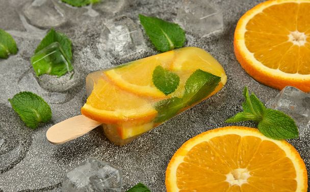 新鮮なオレンジ色のスライス、緑のミントの葉と灰色のテーブルの表面に氷のキューブと1つのフルーツアイスクリームのアイスのアイスのアイスのアイスのアイスのケップルを閉じます。 - 写真・画像
