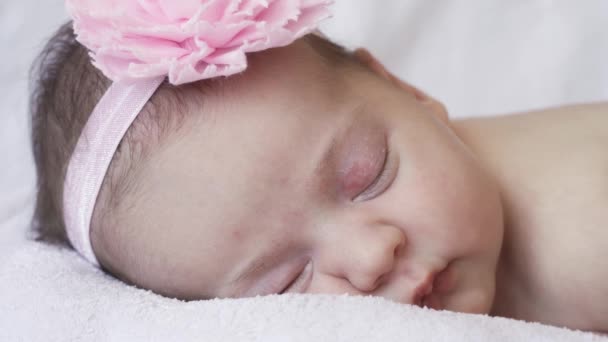 幼児期、子供時代、発達、医学と健康の概念-ピンクの背景に包帯と彼女の頭の上の花で彼女の胃の上に横たわる新生児の裸の眠っている赤ん坊の少女のクローズアップ顔. - 映像、動画