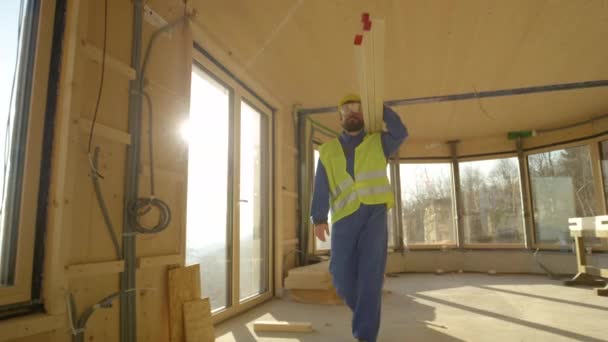 LOW ANGLE: Pracownik przychodzi do pracy niosąc ciężkie drewniane belki na ramieniu - Materiał filmowy, wideo