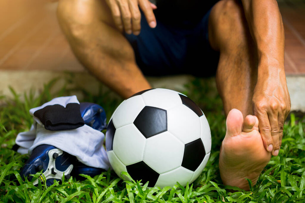 Футбольный мяч и спортивная обувь на зеленой траве с футболистом поймать лодыжку ног из-за боли. Футболист получил травму стопы от боли во время соревнований или тренировок. - Фото, изображение