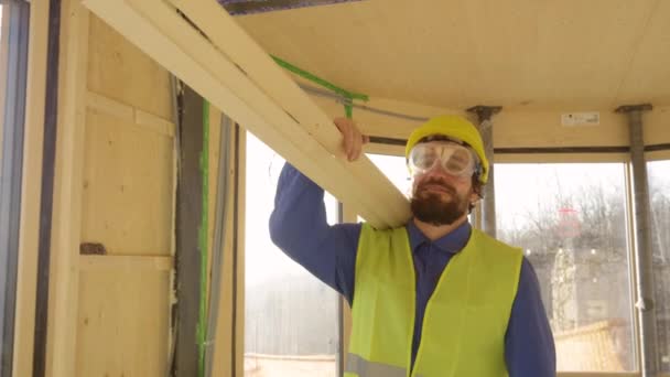 LENS FLARE: Smiling contractor in blue workwear carries planks across a house - Séquence, vidéo