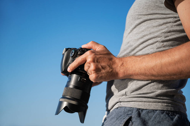 Widok z bliska męskiego fotografa sprawdzającego ustawienia na ekranie aparatu stojącego na zewnątrz pod błękitnym niebem. - Zdjęcie, obraz