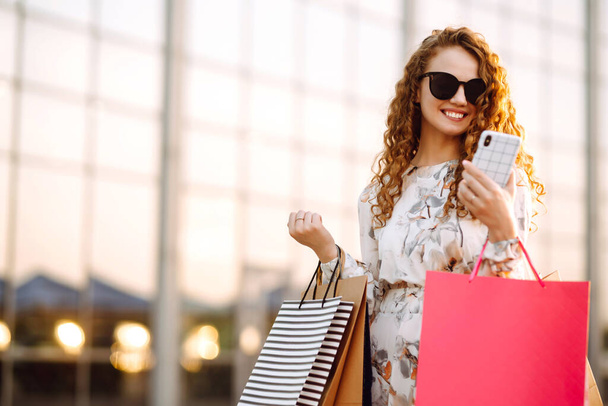 Woman in shopping. Young girl with telephone enjoying shopping in the city street. Online shopping concept. - Zdjęcie, obraz