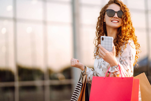 Žena nakupuje. Mladá dívka s telefonem si užívá nakupování na ulici. Koncept nakupování online. - Fotografie, Obrázek