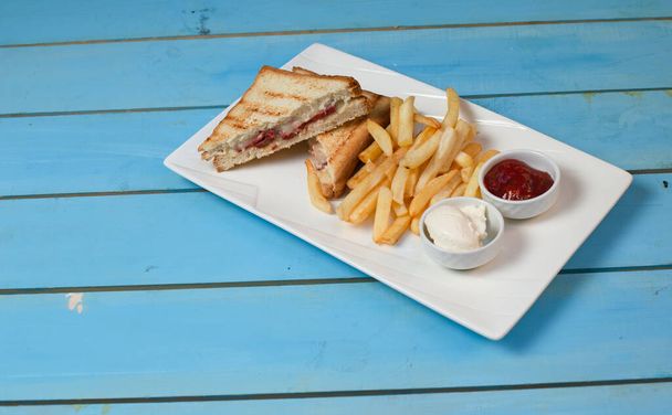 Club sandwiches served with fried potatoes in white plate with ketchup and mayonnaise on blue table - Photo, Image