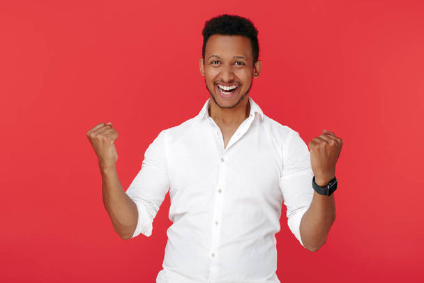 Excited successful african american young man celebrate victory over red background. - Foto, afbeelding