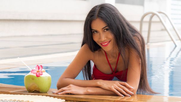asiático tailandés chica sexy en moda ropa interior rojo bikini sentarse en la piscina con bebida coco. - Foto, Imagen