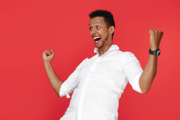 Happy successful african american young man celebrate victory screaming over red background. - Foto, Imagen