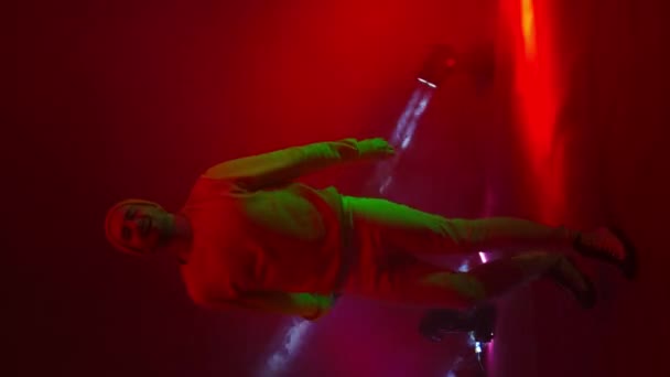 Video verticale. Un artista rap canta in un microfono e balla in luce al neon e luci stroboscopiche luminose nel fumo. Il cantante hip-hop canta energicamente sullo sfondo mutevole dello Studio - Filmati, video