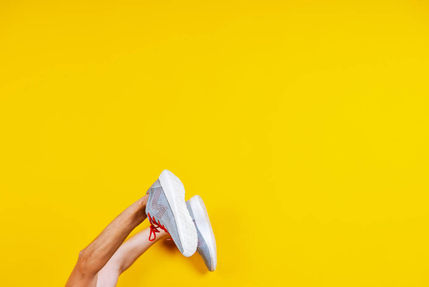 sneakers are worn on hands on a yellow background, red laces, a concept for a fashion blog or magazine, a minimalistic Shoe background, sports - Foto, imagen