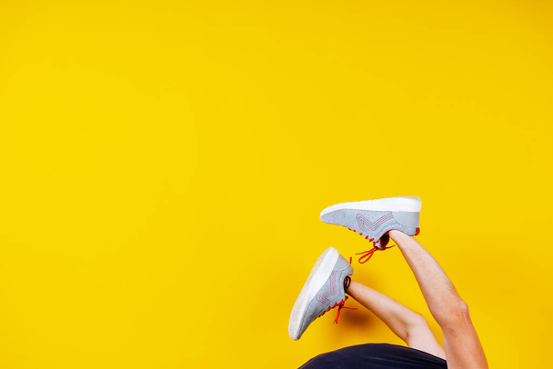 sneakers are worn on hands on a yellow background, red laces, a concept for a fashion blog or magazine, a minimalistic Shoe background, sports - Photo, Image