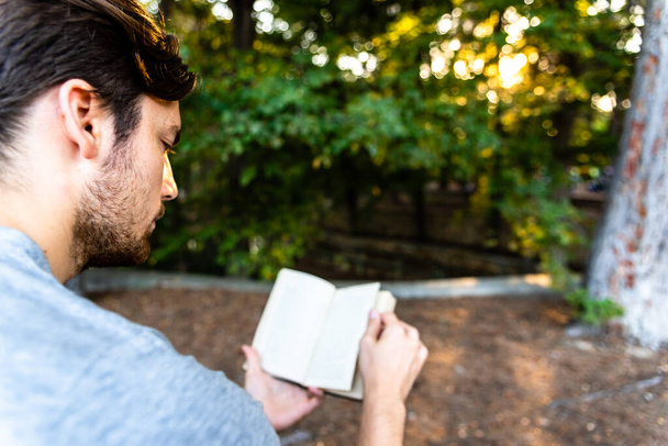 Красивый студент читает книгу, сконцентрированную в открытом парке
. - Фото, изображение