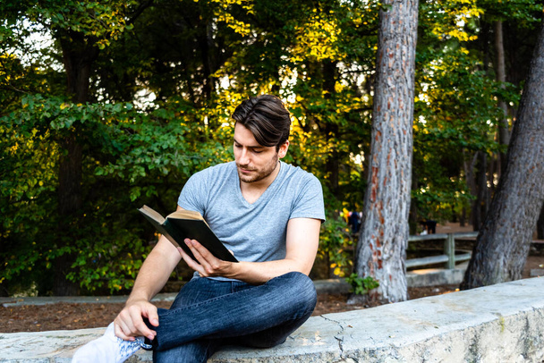 Hezký student čte knihu soustředěnou ve venkovním parku. - Fotografie, Obrázek