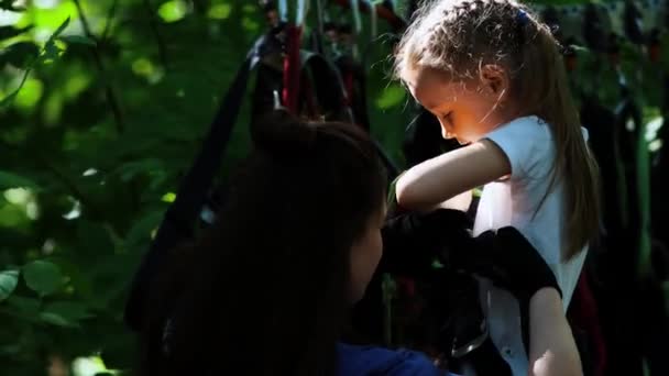Rope adventure - a woman instructor puts on the insurance belt on the waist of a little girl - Footage, Video