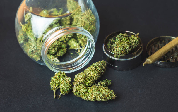 Lékařská marihuana květinové pupeny ve skleněné sklenici a bruska na tmavém pozadí - Fotografie, Obrázek