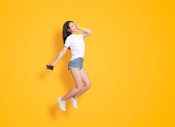  mujer joven saltando mientras escucha música en los auriculares
 - Foto, Imagen