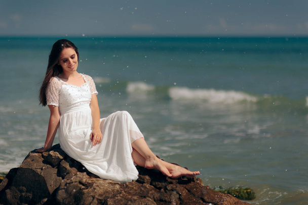 Woman with Long Dress Sitting on Rocks By the Sea - Foto, afbeelding