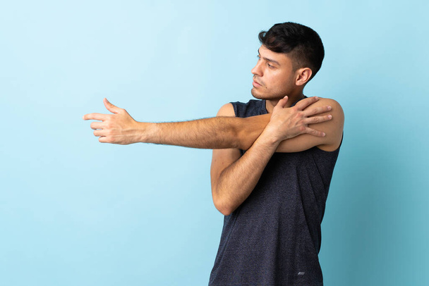 Young Colombian man isolated on blue background stretching arm - Foto, Imagem