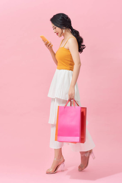Woman carrying shopping bags and text messaging on the phone - Foto, afbeelding