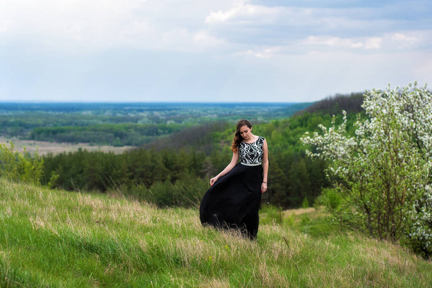 Mulher bonita com vestido preto em um campo verde, desfrutando no dia de primavera
 - Foto, Imagem