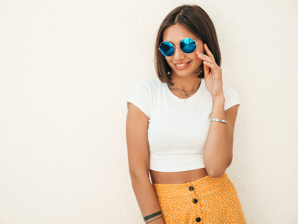 Portrait of beautiful smiling brunette model dressed in summer hipster  clothes. Trendy girl posing in the street near white wall. Funny and positive woman having fun - Φωτογραφία, εικόνα