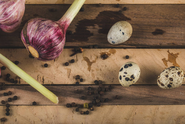 Quail eggs in a small pot with pink garlics and pepper balls on a wooden board - Fotó, kép
