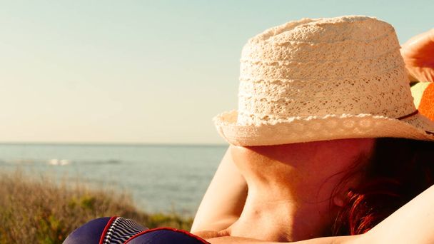 Travel freedom concept. Tourist mature woman relaxing on chair, sunbathing, enjoying summer beach vacation. Face covered with hat. - Photo, image