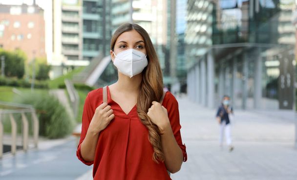 Mladá žena v ochranné masce KN95 FFP2 kráčí v moderní městské ulici. Studentka s obličejovou maskou proti Coronavirové nemoci 2019 (COVID-19). - Fotografie, Obrázek