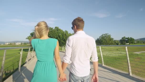 CLOSE UP: Unrecognizable couple holding hands walks across a bridge in a park. - Footage, Video