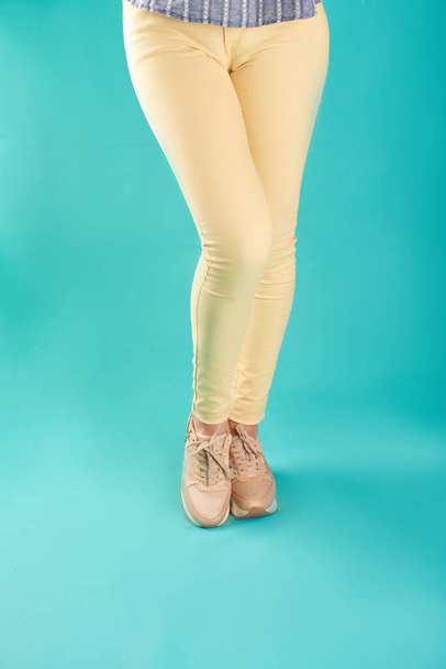 Close up photo of sneakers and yellow skinny jeans against an aqua background in a studio. - Фото, изображение